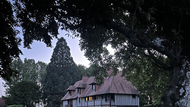 Ein traditionelles Fachwerkhäuschen mit gepflegtem Rasen und einem Baum im Vordergrund.