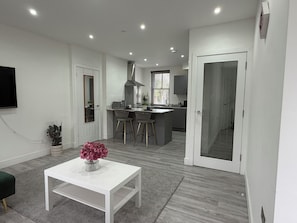 Una cocina moderna con barra, una mesa de comedor blanca con un florero y un suelo alfombrado en tono gris.