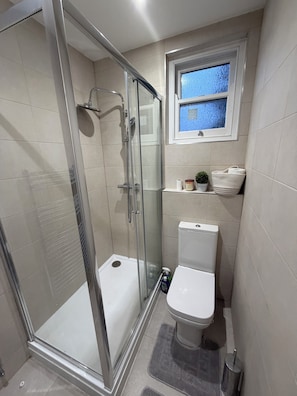 Un baño con ducha de vidrio, inodoro y una ventana pequeña.