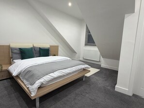 Une chambre moderne avec un plafond en pente, un lit recouvert de linge de lit blanc et un tapis gris.