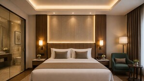 A modern hotel room with a large bed, bedside lamps, a green armchair, and a small table with a plant.