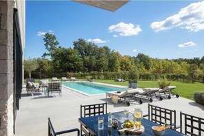 Ein Poolbereich im Freien mit Liegestühlen, einem Tisch mit Getränken und Blick auf einen üppigen Garten.