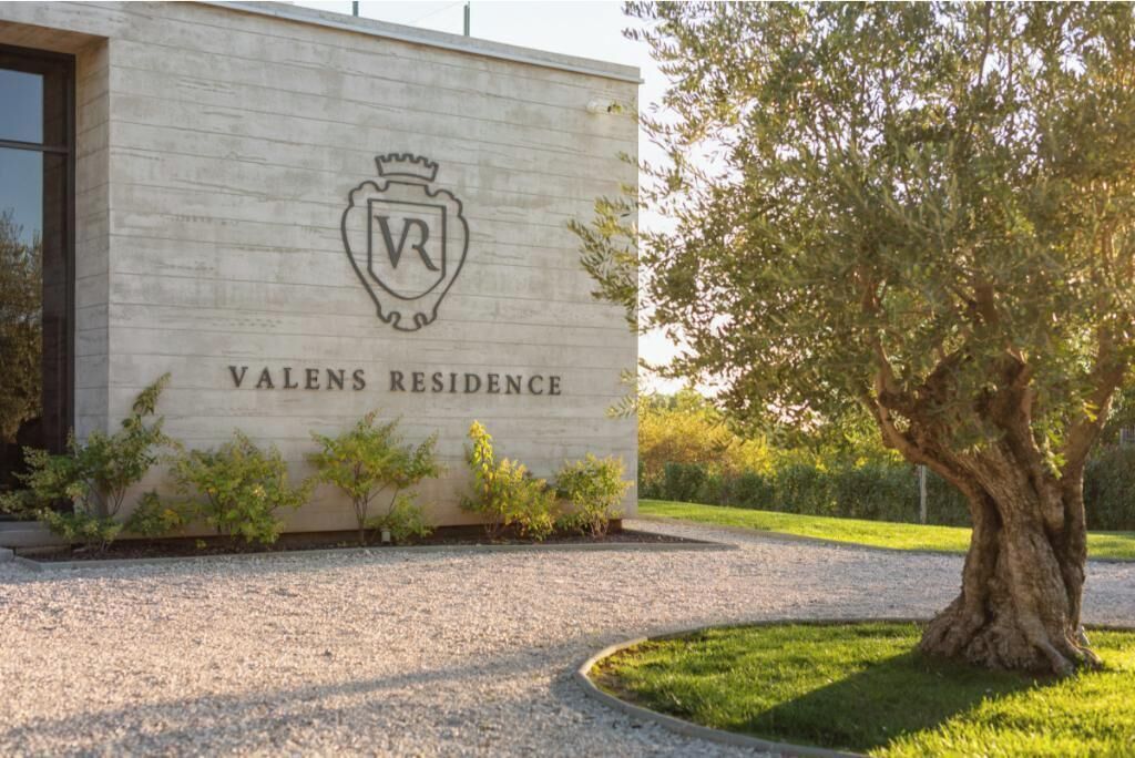 Un edificio con un letrero que dice 'VALENS RESIDENCE' y un logotipo con escudo.