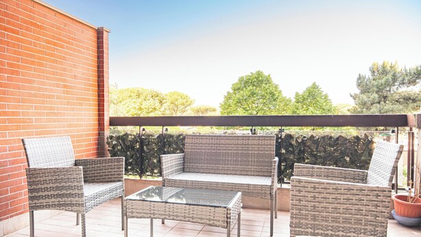 An outdoor patio with wicker furniture and a glass table, a brick wall, and a view of trees. - Roman Urban Stay (Roma)