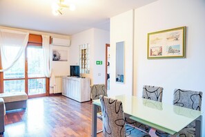Ein modernes Wohnzimmer mit Essbereich, großen Fenstern, einem Fernseher und einem gerahmten Bild an der Wand.