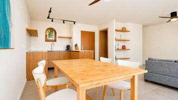 A modern kitchen with wooden cabinets, a dining table with chairs, a grey sofa, and a ceiling fan.