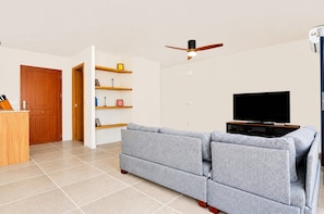 A living room with a sofa, TV, ceiling fan, wooden door, and shelves.