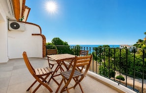 A balcony with a table and chairs, overlooking a coastal view.
