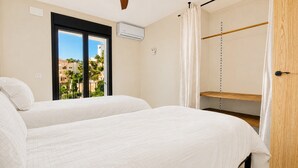 Habitación de hotel con dos camas, ventana con vistas a edificios, un equipo de aire acondicionado y una puerta de madera.