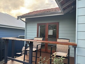 Eine Terrasse mit Tisch und Stühlen, eine Schiebetür und ein blaues Gebäude im Hintergrund.