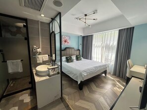 A modern hotel room with a large bed, a separate bathroom, a desk, and a window with curtains.