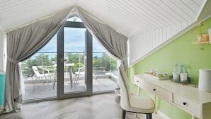 Ein Zimmer mit schrägverdeckter Decke, einer Schiebeglas-Tür zu einem Balkon, einem weißen Schreibtisch mit Schubladen und einer grünen Wand.