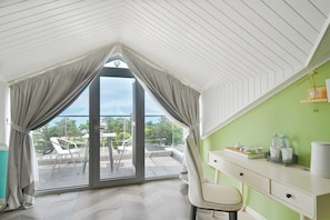 A room with a sloped ceiling, a sliding glass door to a balcony, a white desk with drawers, and a green wall. - Encounter Villa Art  Garden Homestay (Qingdao)