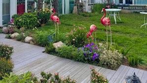 Ein modernes Haus mit Wintergarten, Holzterrasse und gepflegtem Garten mit Flamingos.