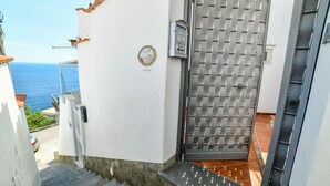 En trappe fører op til en dør med et jerngitter, en postkasse og udsigt til havet.
