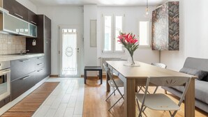 A modern kitchen with dark cabinets, a wooden dining table, and a gray sofa. - Casa Centotrecento by Wonderful Italy (Bologna)