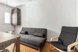 A modern room with a grey sofa, a wooden chair, a dining table, and a wall with a leaf-patterned artwork. - Casa Centotrecento by Wonderful Italy (Bologna)