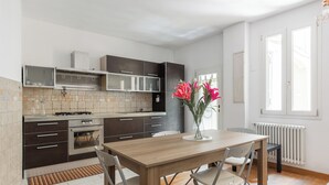 A modern kitchen with dark cabinets, a wooden dining table, and a vase with flowers. - Casa Centotrecento by Wonderful Italy (Bologna)