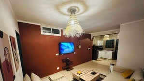 Een woonkamer met een bank, salontafel, televisie en een keuken op de achtergrond.
