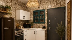 Een keuken met een koelkast, fornuis, oven, kastjes, een hanglamp en een deur met een bordje.