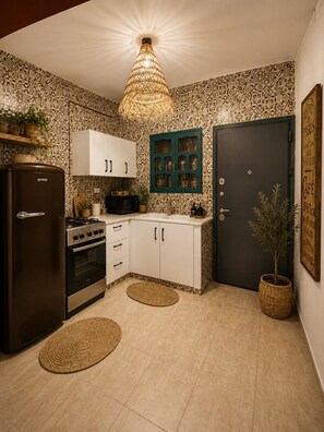 Uma cozinha com geladeira, fogão, forno, armários, luminária pendente e uma porta com uma placa.