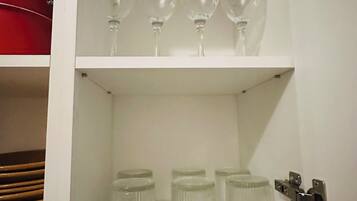 Un mueble blanco con copas de vino en la repisa superior y frascos de vidrio en la inferior.
