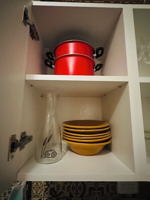 Un meuble de cuisine contenant une casserole rouge, des assiettes jaunes et un pichet en verre transparent.
