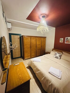 Quarto com cama, guarda-roupa de madeira, espelho, luminária pendente e uma pequena mesa.