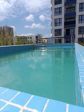 Ein Pool auf dem Dach mit klarem, blauem Wasser, umgeben von modernen Gebäuden und einem wolkenlosen Himmel.