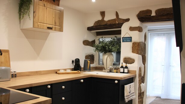 A kitchen with a wooden countertop, black cabinets, a coffee maker, and a sign reading 'Welcome to The Sails.' - The Sails – Romantic Retreat for Two, Cosy Light-Filled House (Leek)
