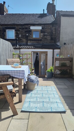 A patio with a checkered tablecloth, a patterned rug, and a wooden bench. - The Sails – Romantic Retreat for Two, Cosy Light-Filled House (Leek)