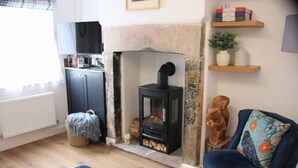 A living room with a fireplace, a blue sofa, a wooden cabinet, and a television. - The Sails – Romantic Retreat for Two, Cosy Light-Filled House (Leek)
