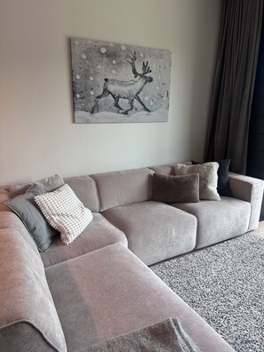 Ein modernes Wohnzimmer mit einem grauen Ecksofa, einer Decke und einem dekorativen Wandbild.