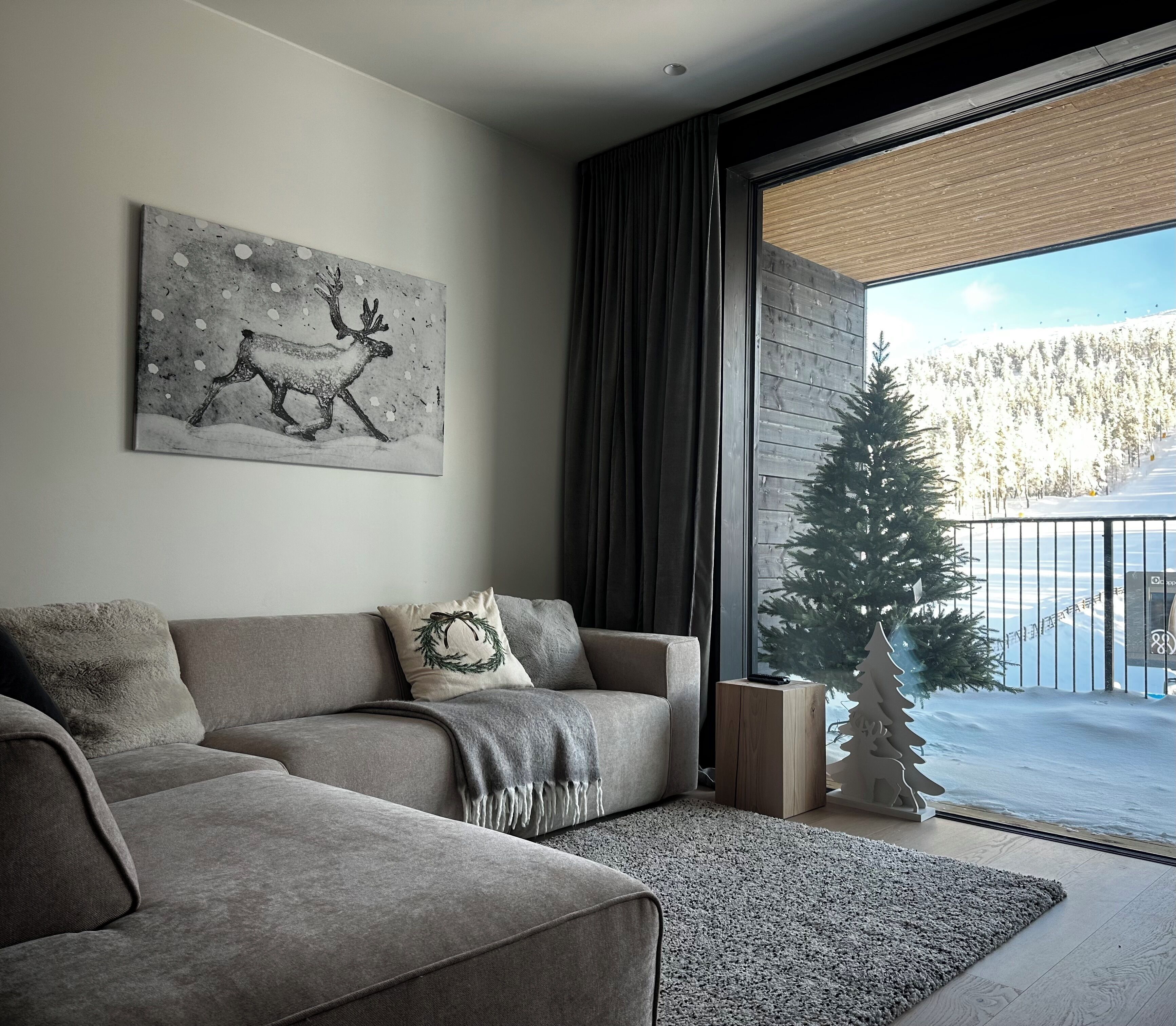 A modern living room with a grey sofa, a fireplace, and a view of a snowy landscape through a large window.