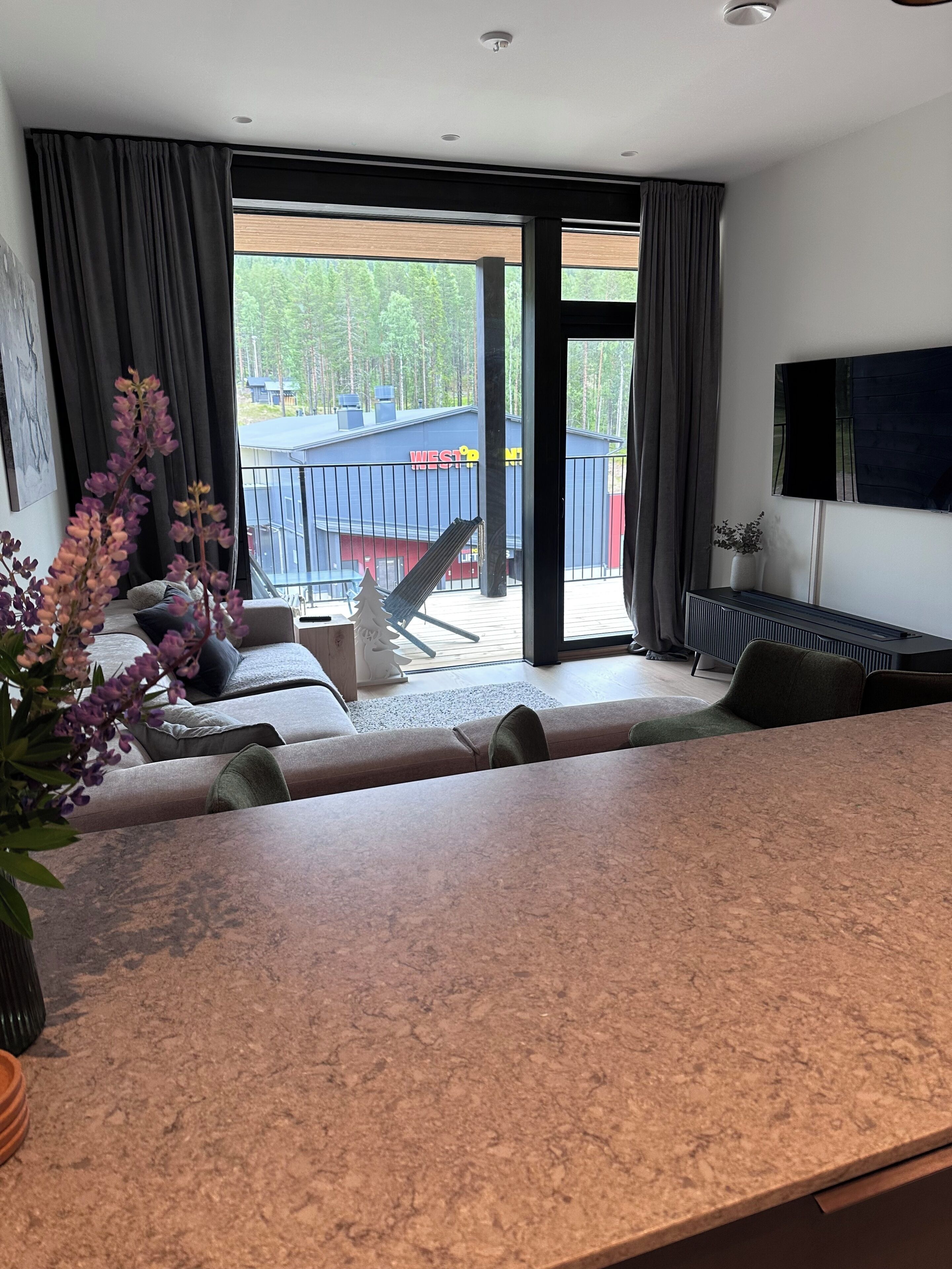 Un salon moderne avec une grande fenêtre, un canapé, une table basse et un téléviseur.