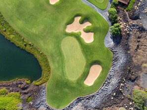 Luchtbeeld van een golfbaan met zandbunkers, een waterpartij en een gebouw.