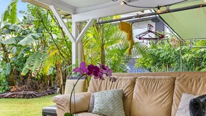 A beige sofa with cushions, a small table, and a hanging light fixture in a lush garden setting.