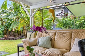 A beige sofa with cushions, a small table, and a hanging light fixture in a lush garden setting. - Historic Hilo Plantation Oasis w/ Tropical Gardens (Hilo)