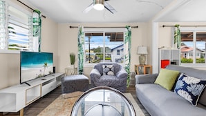 A living room with a ceiling fan, a TV, a sofa, a chair, and a glass coffee table.