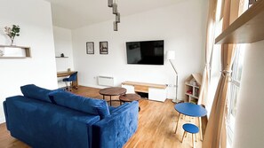 A modern living room with a blue sofa, a TV, a desk, and a bookshelf. - Wonderful 2-bedroom penthouse apartment in peaceful Southampton near local spots (Southampton)