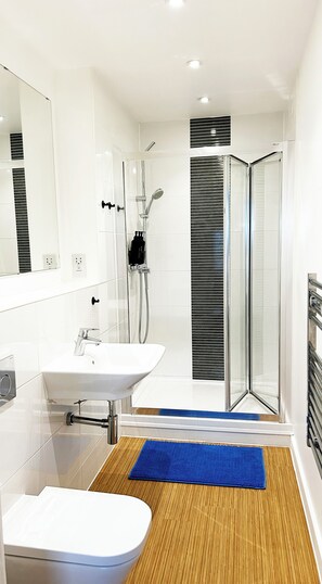 A modern bathroom with a glass shower enclosure, a white sink, and a blue bath mat. - Wonderful 2-bedroom penthouse apartment in peaceful Southampton near local spots (Southampton)