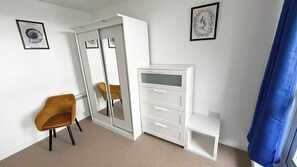 Ein Zimmer mit Schrank, Stuhl, Schreibtisch und zwei gerahmten Bildern an der Wand.
