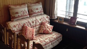 Una habitación con paneles de madera, un sofá y sillones, una ventana con cortinas y un radiador.