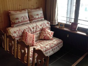 A wooden paneled room with a sofa and chairs, a window with curtains, and a radiator. - Beautiful Flat Facing La Clusaz Slopes (La Clusaz)