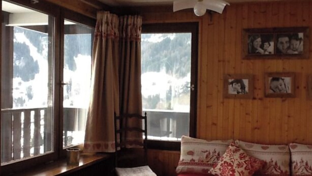 Una habitación acogedora con detalles de madera, un sofá rojo, una ventana con cortinas y cuadros enmarcados en la pared.