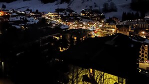 Vista nocturna de una montaña nevada con un pueblo en la falda, con edificios iluminados y una pista de esquí.