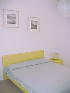 Ein Zimmer mit einem Bett, einem Nachttisch und zwei gerahmten Bildern an der Wand.