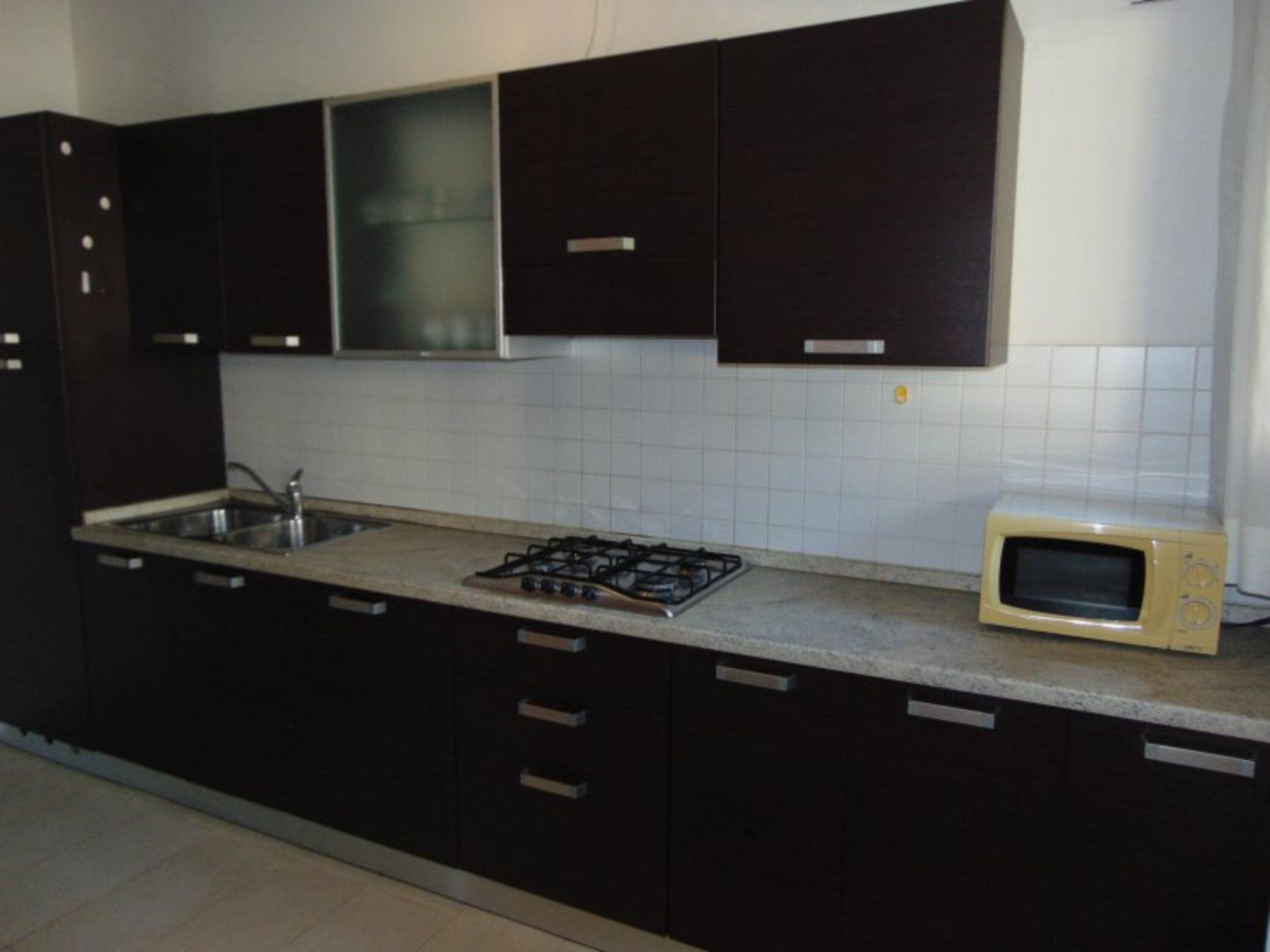 A kitchen with dark cabinets, a gas stove, a sink, and a microwave.