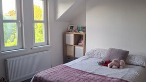 A bedroom with a bed, a window, a radiator, a shelf with items, and a ceiling light. - House Sleeps 6 With Wifi (Belfast)