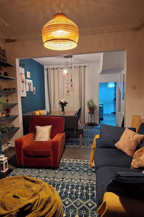 Een woonkamer met een rode fauteuil, een zwarte bank, een kamerkleed met patroon en een hanglamp.